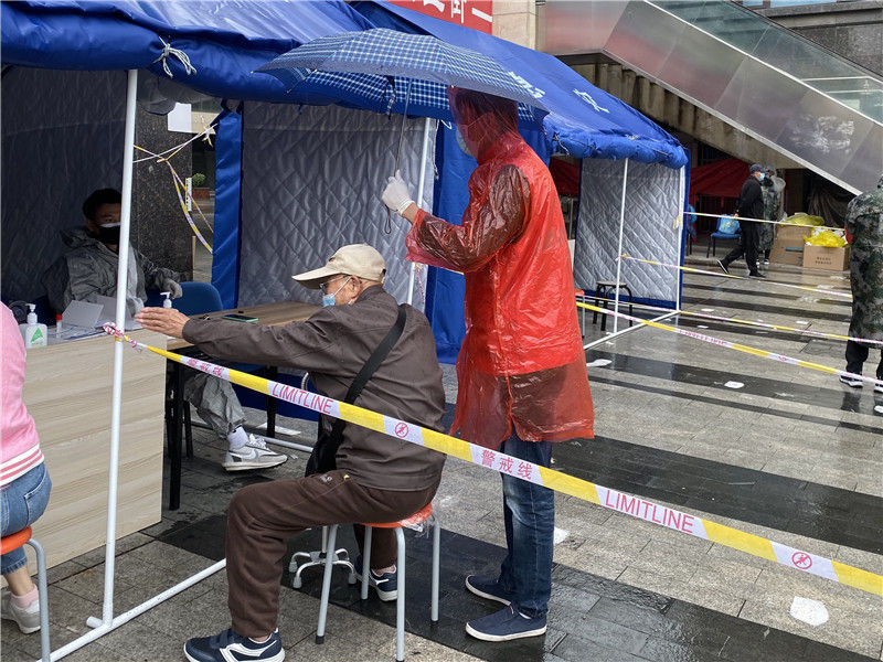 尚樂城廣場檢測點，身穿紅馬甲的社區志願者為等待檢測的老人打傘。