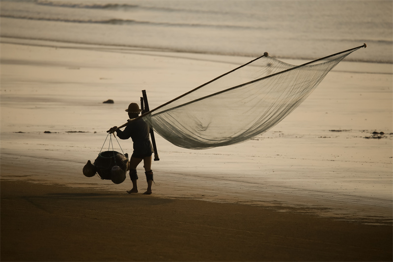 日照市兩城街道漁民扛著捕蝦走在沙灘上，身影與朝霞相映成趣。張明慷  攝