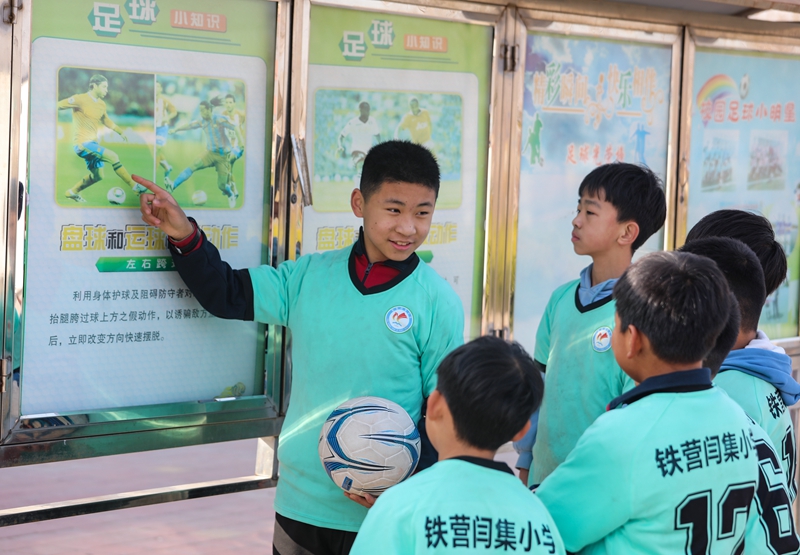 12月6日，學生們在鐵營鎮閆集小學足球場文化欄前分享足球知識。