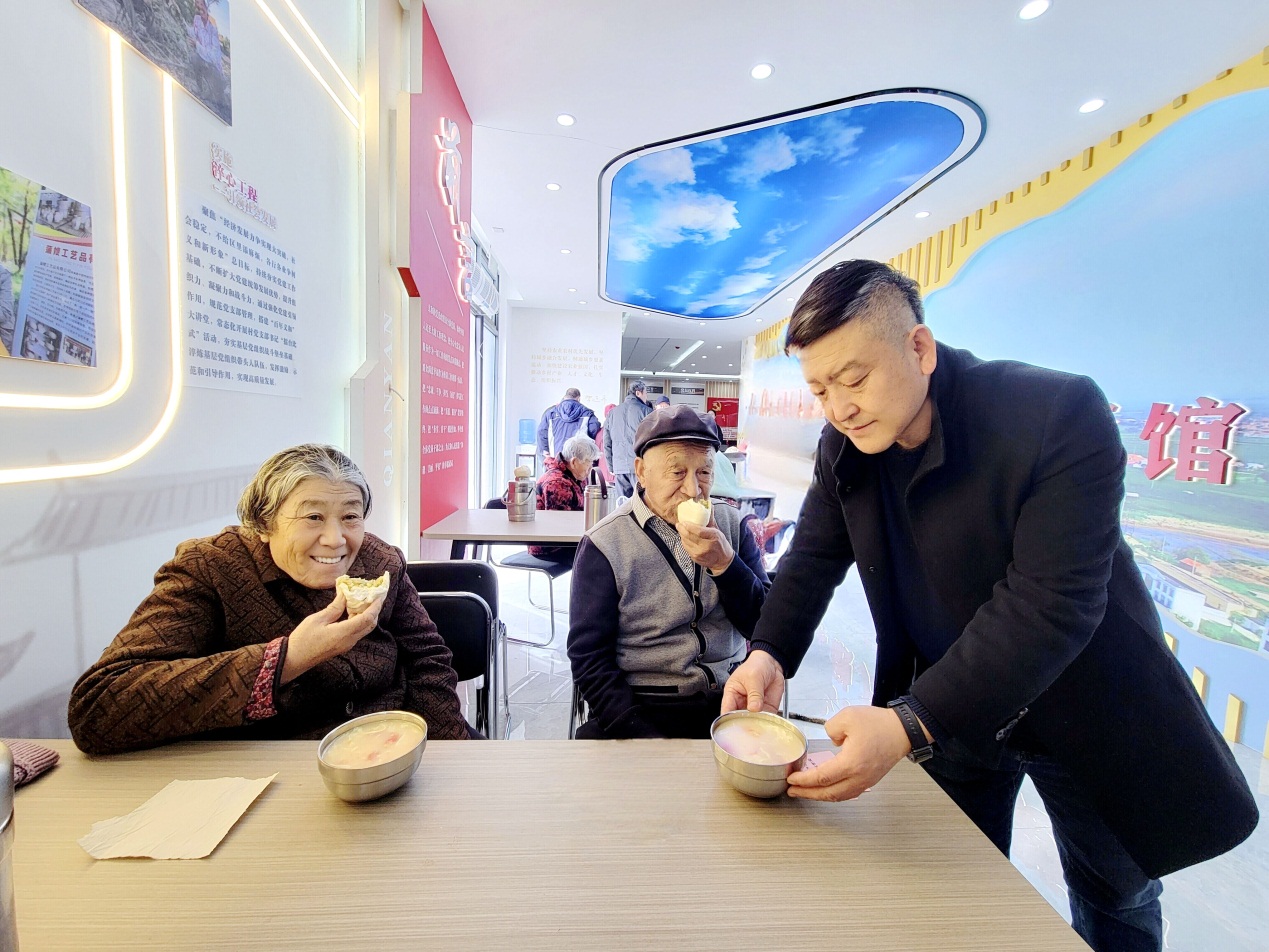 图为第一书记李国军（右一）为幸福食堂就餐老人添汤
