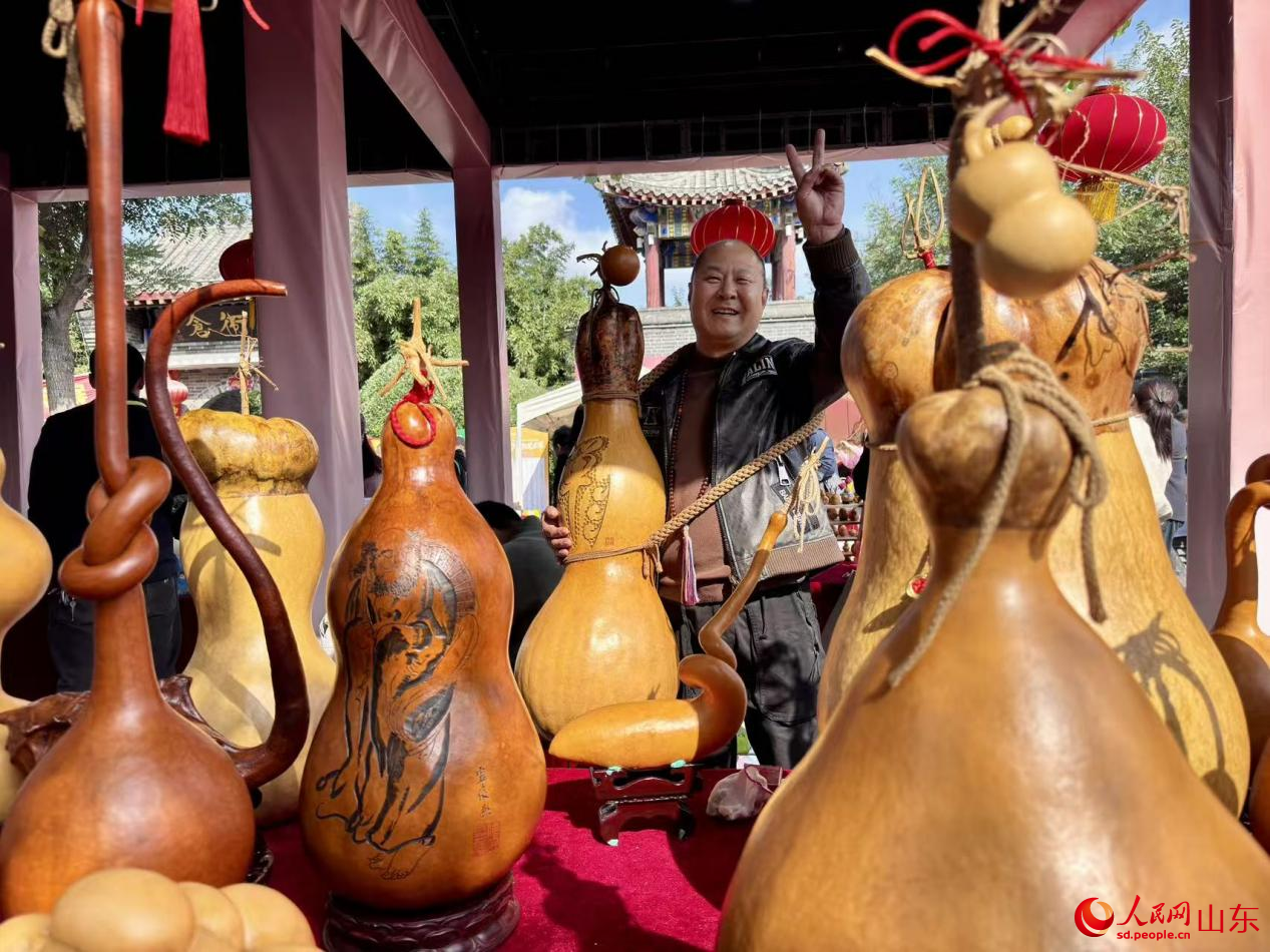 身挂大葫芦工艺品的摊主正向游客展示自己心爱的宝贝。人民网 郑昕桥摄