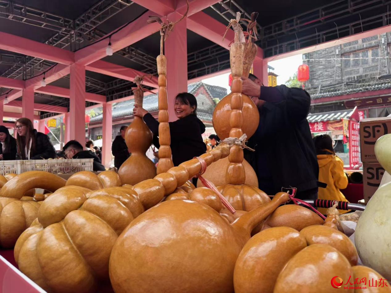 两位摊主满面笑容,正在认真擦拭葫芦工艺品。人民网 郑昕桥摄