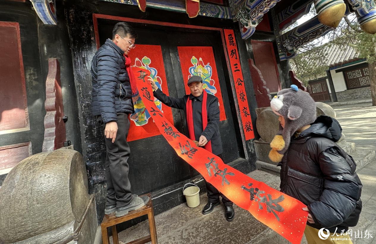 在孔府重光门前，全国文明家庭代表孔令绍祖孙三代演示春联与门神张贴过程。人民网记者 乔姝摄