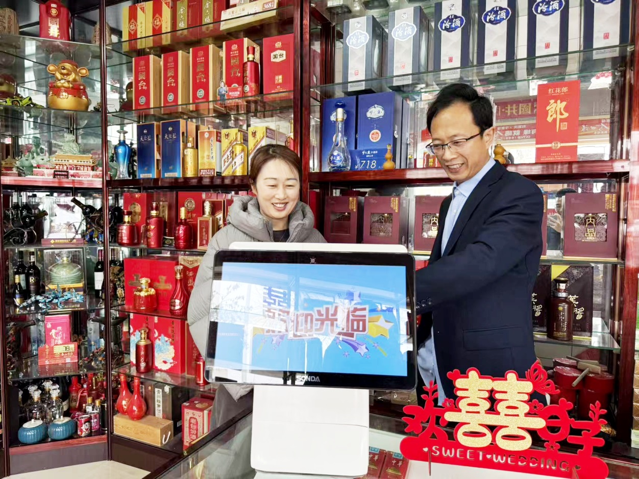 客户经理盖海峰(右一)指导恒达烟酒商行店主董婷使用店铺管理系统盘点商品